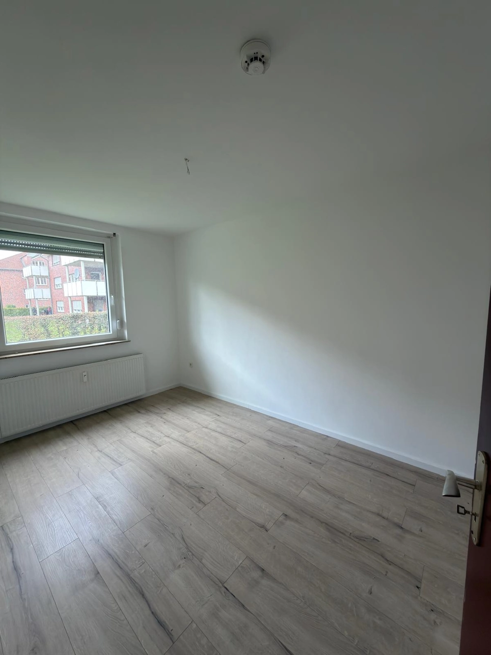 Leeres Zimmer mit frisch gestrichenen weißen Wänden, neu verlegtem Laminatboden und Fenster mit Heizkörper darunter, Laminat verlegen