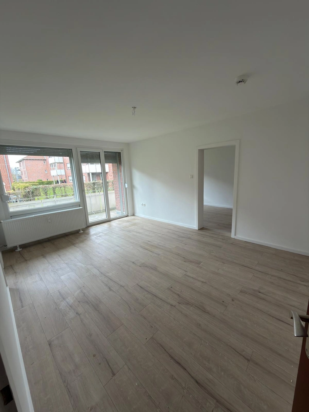 Leeres Wohnzimmer mit hellen Laminatdielen, weißen Wänden und Balkonzugang – Laminat verlegen