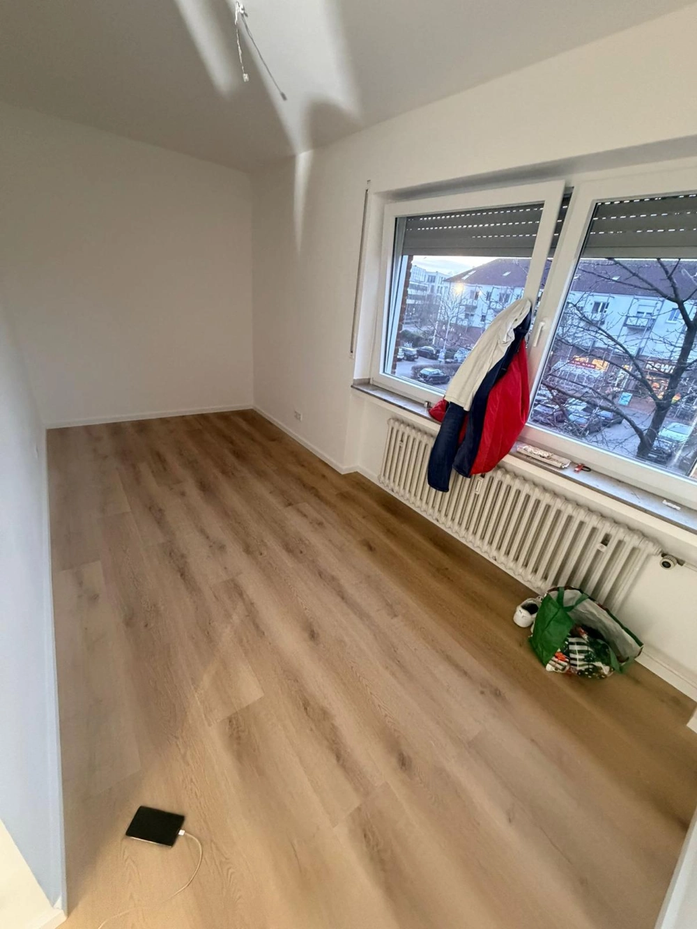 Laminat verlegen: helles Zimmer mit frisch verlegtem Laminatboden, weißen Wänden und Fenster mit Heizkörper