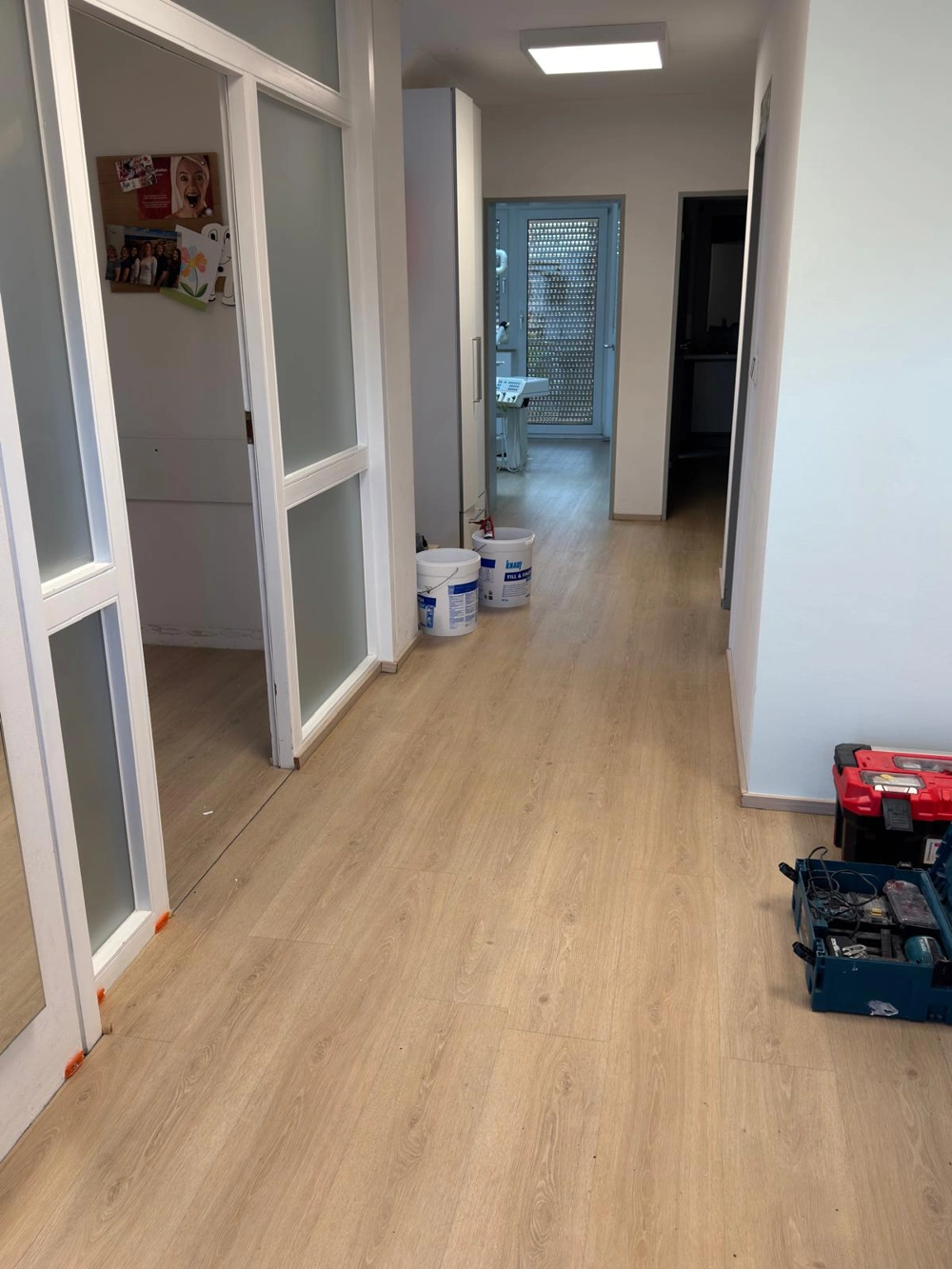 Flur mit neu verlegtem Laminatboden, weißen Wänden, Glasschiebetüren, Spachtel-Eimern und Werkzeugen für Laminat verlegen
