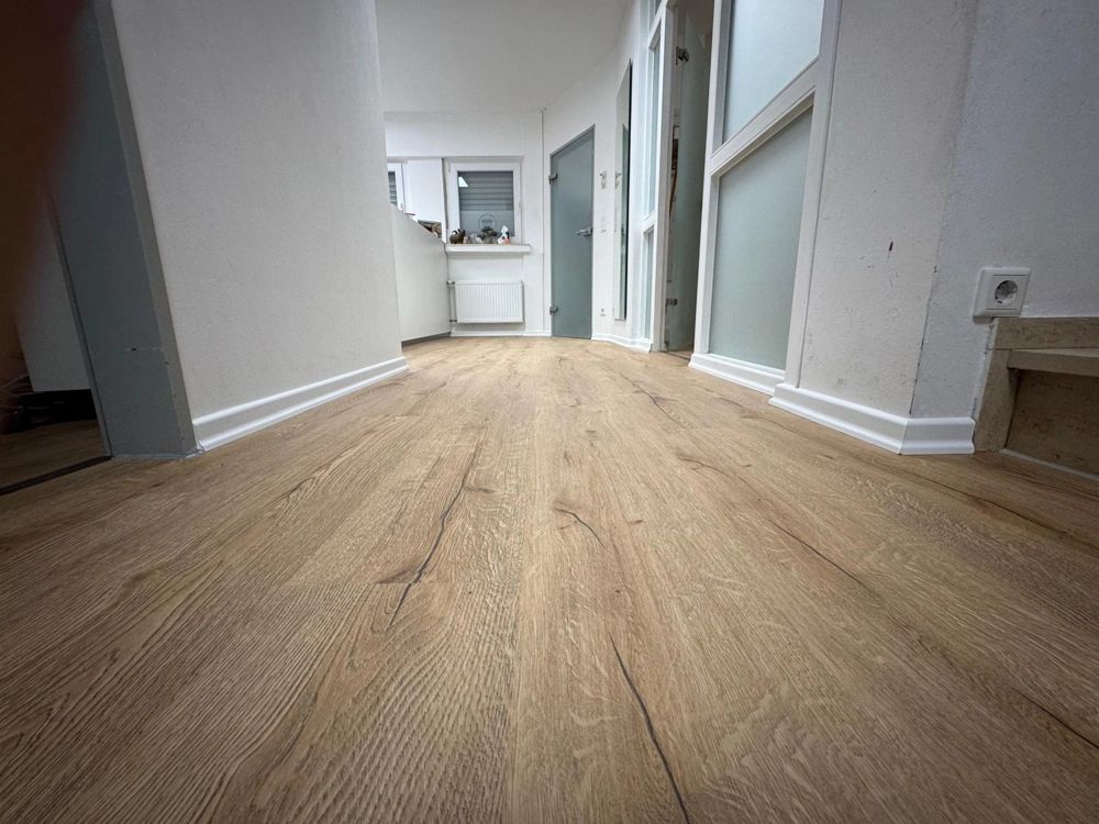 Flur mit frisch verlegtem Vinylboden in Holzoptik und weißen Sockelleisten – Vinylboden verlegen