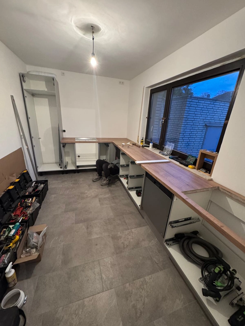 Teilmontierte Küchenunterschränke und Arbeitsplatte in modernem Raum mit Werkzeugen und offener Fensterfront (Küchenrenovierung)