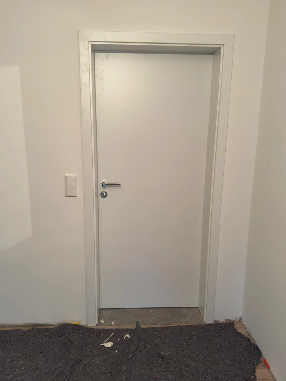 Weiß eingebaute Innentür mit modernem Drücker, roh verlegter Boden und Wand, Türen montieren