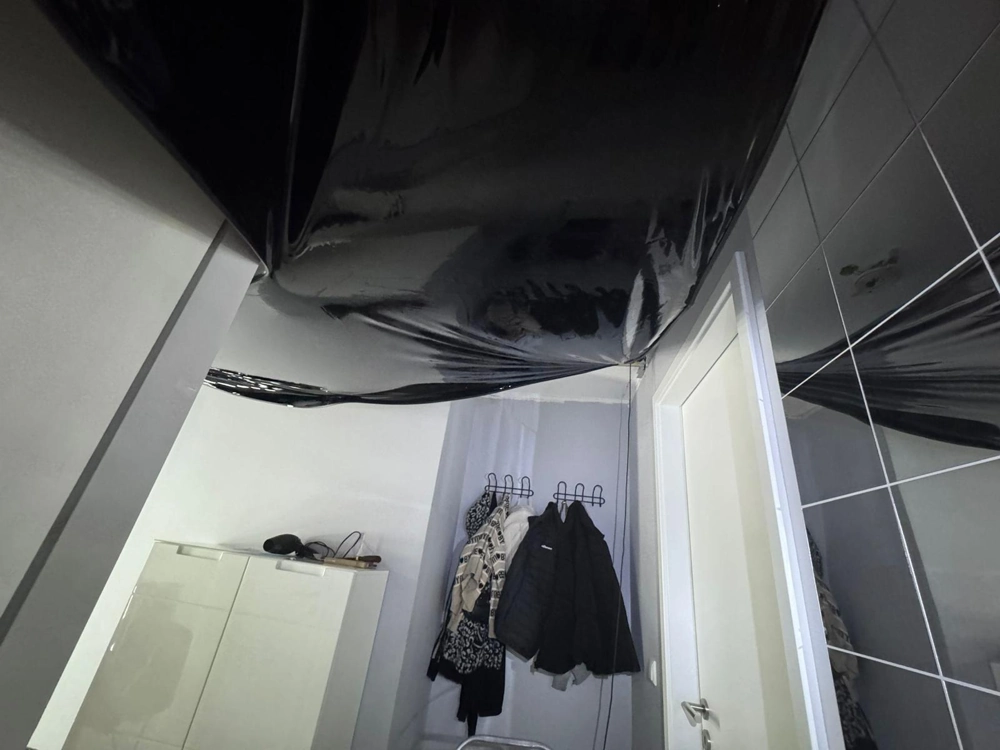 Schwarze Spanndecke in der Sanierung eines Flurs mit Garderobe, gespachtelten Wänden und offener Tür
