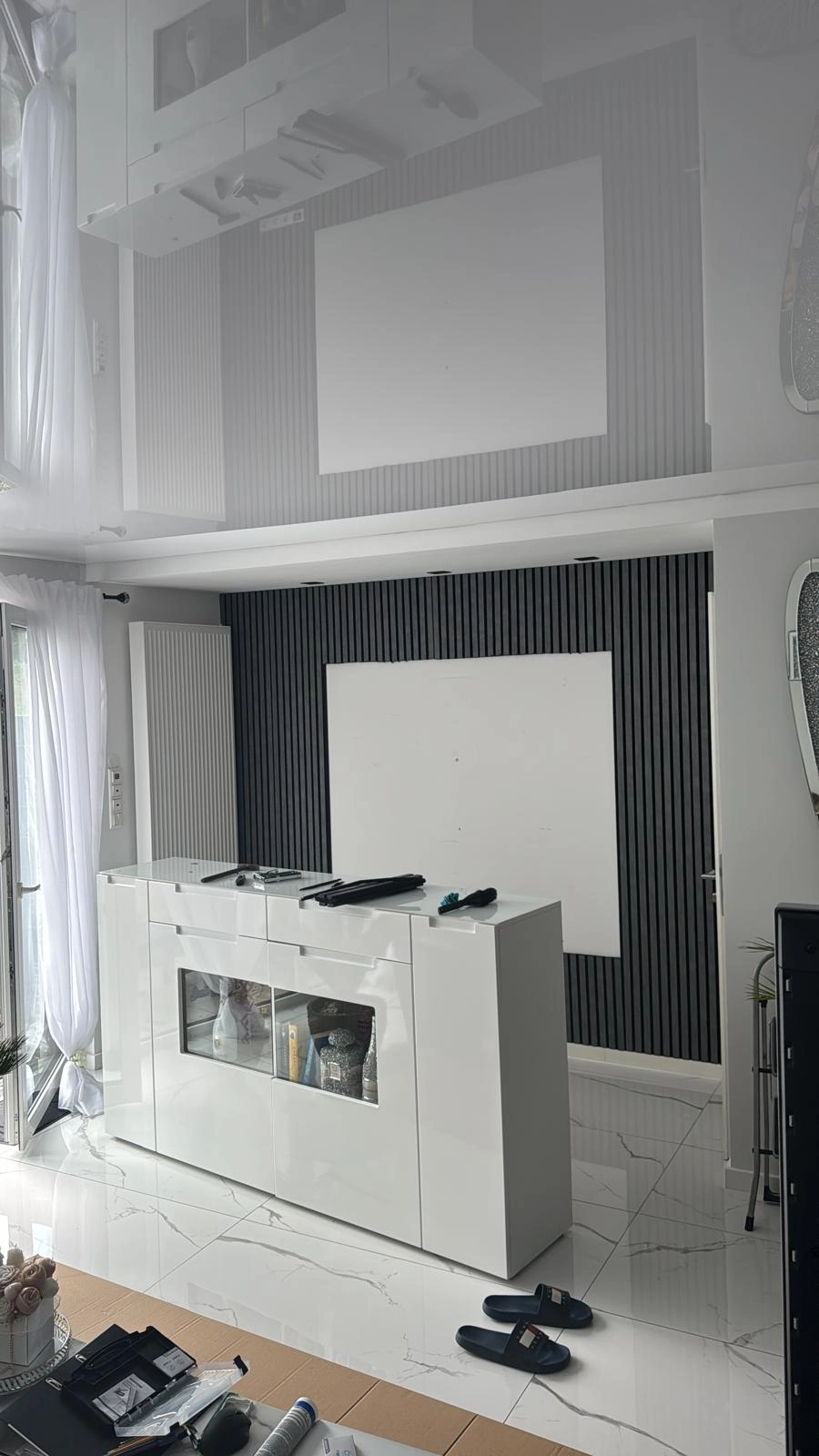 Reflektierende Spanndecke über modernem Wohnzimmer mit weißem Highgloss-Sideboard und schwarzer Rippwand