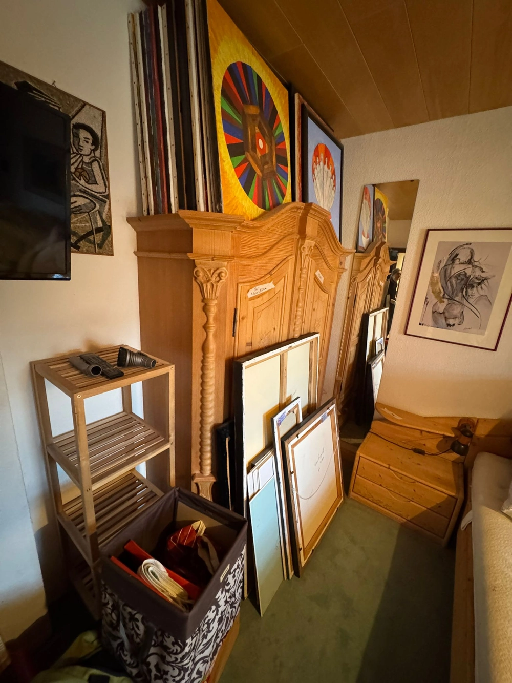 Entrümpelung: Antiker Holzschrank, Regale, Kisten und gerahmte Bilder an einer Wand gestapelt