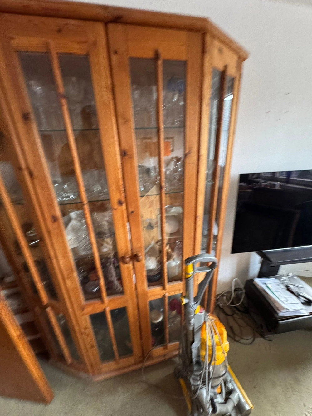 Holzvitrine mit Glasgeschirr und aufgestelltem Staubsauger bei Entrümpelung