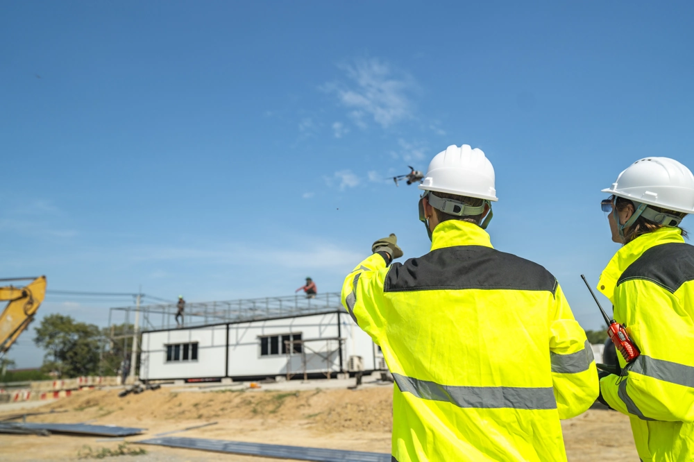 Baustelleninspektion per Drohne durch Generalunternehmer in Warnschutzkleidung vor Rohbau