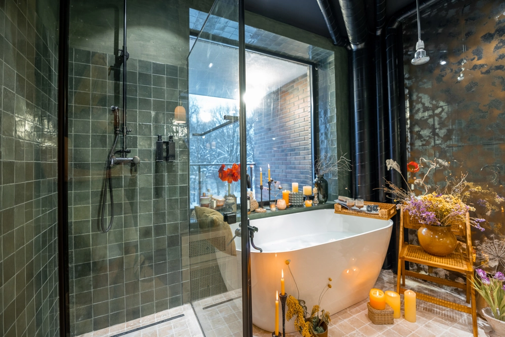 Freistehende Badewanne in stilvoller Badsanierung mit begehbarer Dusche, dunklen Wandfliesen, Kerzen und Pflanzen