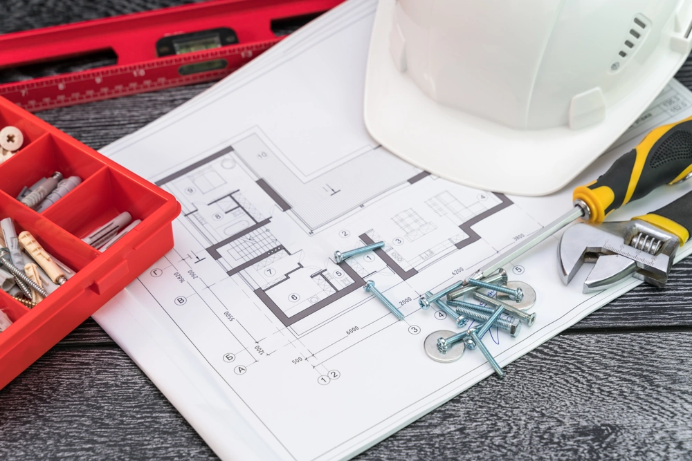 Werkplan auf Schreibtisch mit Bauhelm, Schrauben, Schraubendreher und Zollstock für Trockenbau