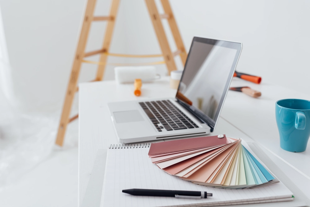 Arbeitsplatz mit Laptop, Farbkarte und Malerwerkzeug für Malerarbeiten
