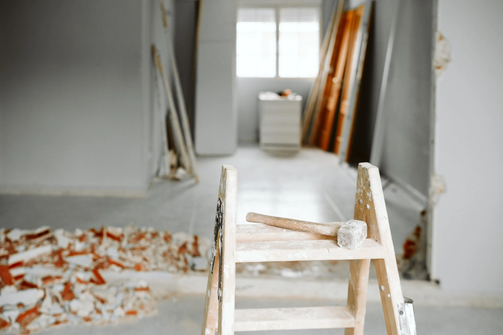 Leiter mit Hammer vor abgebrochener Wand und Schutt auf Boden bei Abbrucharbeiten