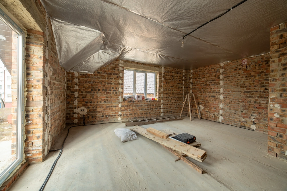Unrenovierter Rohraum mit Backsteinwänden und Foliendämmung beim Trockenbau