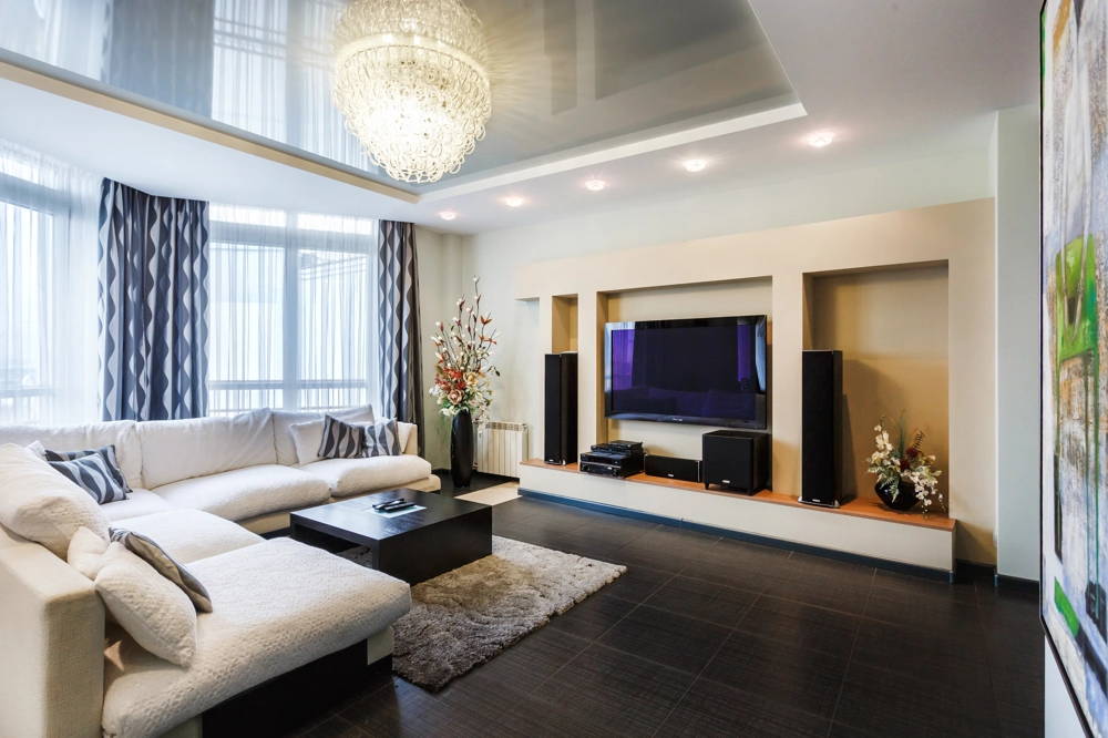 Modernes Wohnzimmer mit Einbauschrank, weißem Ecksofa, schwarzem Couchtisch und glänzenden Spanndecken