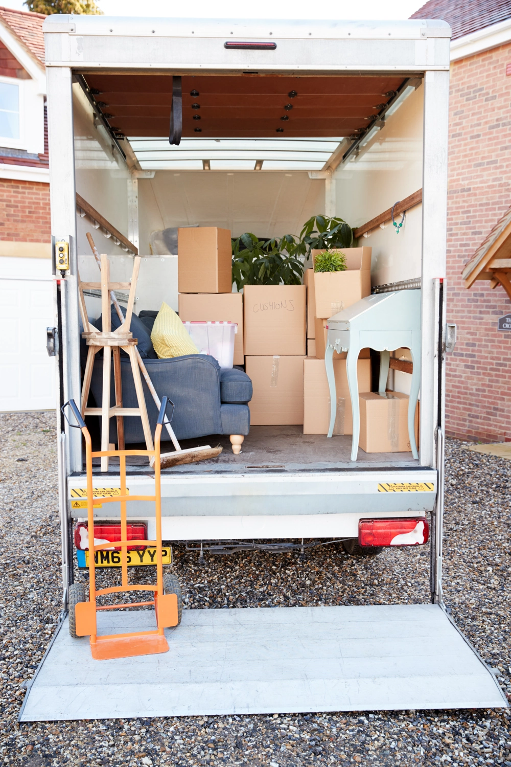 Offener Lkw für Umzüge mit Kartons, Möbeln und Sackkarre vor einem Wohnhaus