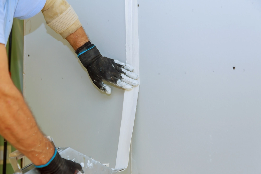 Hände eines Handwerkers führen Spachtelarbeiten an einer Trockenbauwand aus