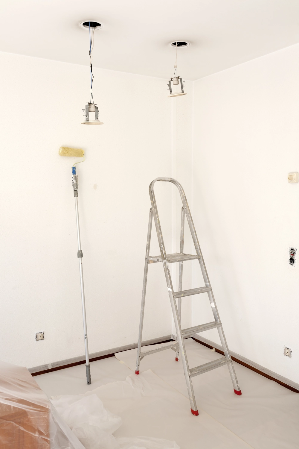 Raum-innenausbau mit Malerarbeiten: weiße Wände, Farbroller, Leiter und abgehängte Decke mit vorbereiteten Deckeneinbauleuchten