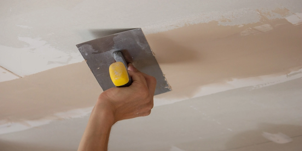 Hand glättet Decke mit Kelle bei Spachtelarbeiten im Innenausbau